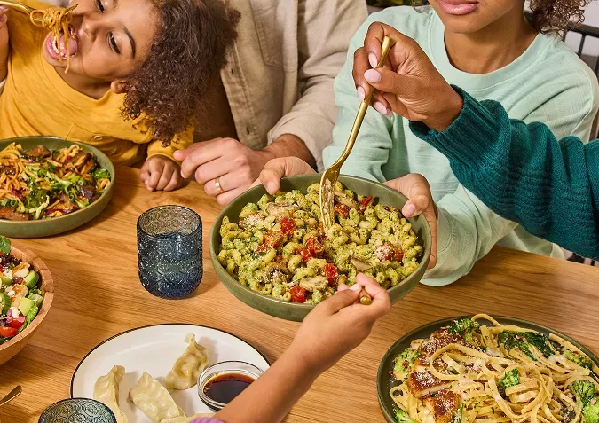 Family enjoying noodles dishes like basil pesto cavatappi, potstickers and crispy chicken bacon alfredo.
