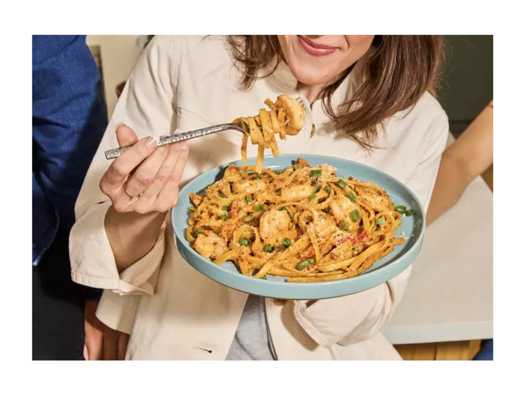 Woman eating Cajun Shrimp Fettuccine on a blue plate.