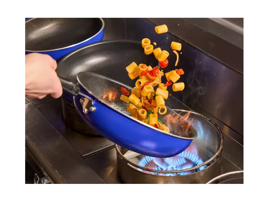 Rigatoni rosa noodle dish being sautéed in a blue pan over a flame.