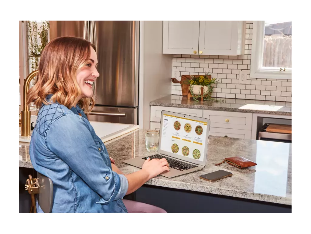 Woman ordering Noodles &amp; Company on her computer in her kitchen.