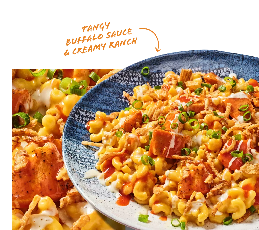Tangy Buffalo Sauce &amp; Creamy Ranch. Noodles &amp; Company's Buffalo Chicken Ranch Mac shown on a blue plate with a close-up of cheesy noodles and chicken.