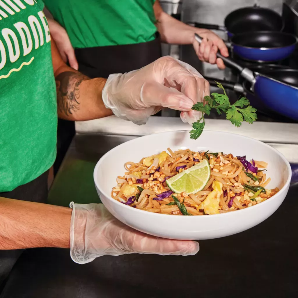 Noodles &amp; Company Team Member garnishing a bowl of Pad Thai with Cilantro