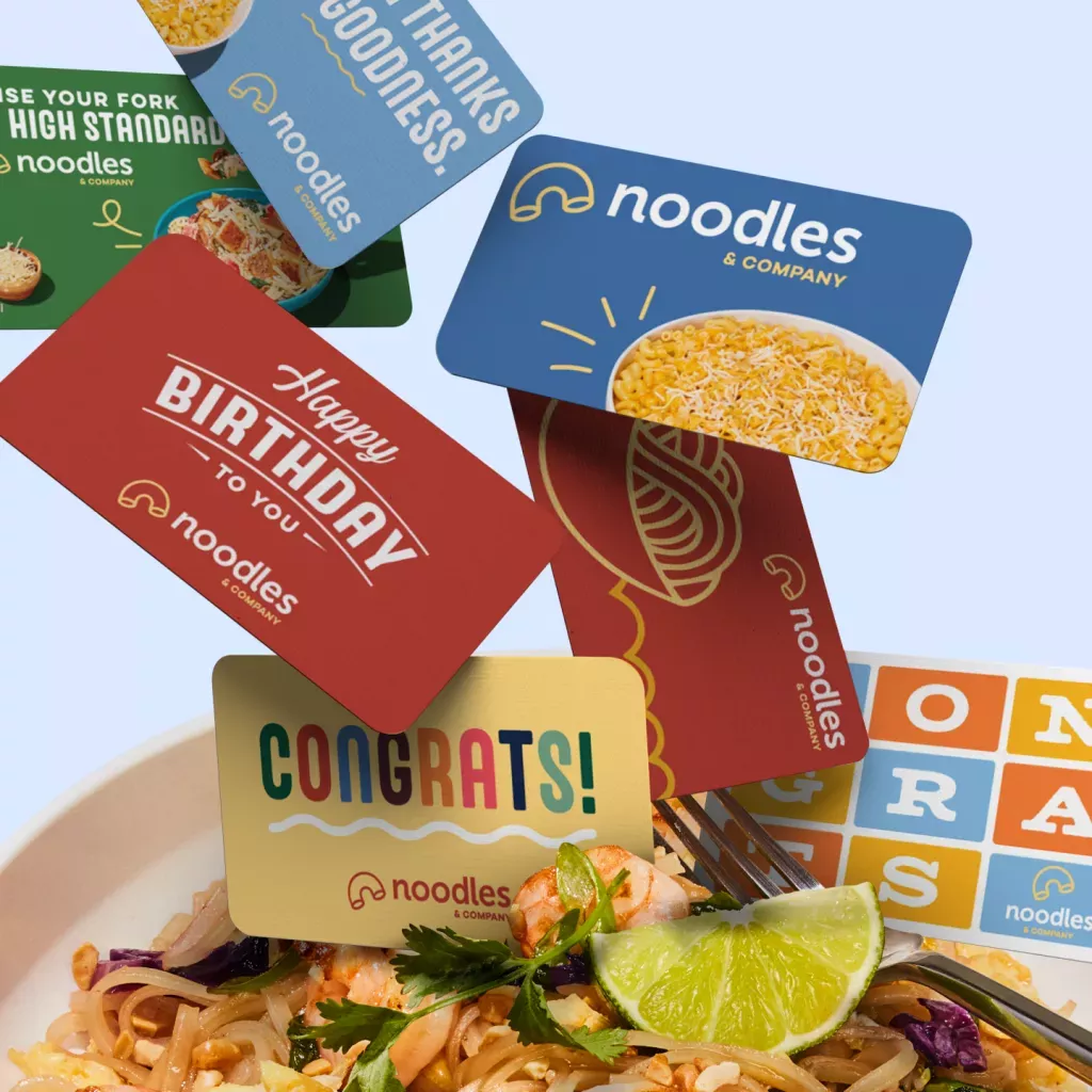 Noodles &amp; Company gift cards falling into a bowl of Pad Thai.