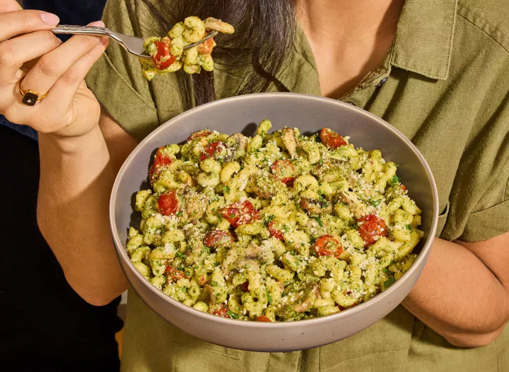 Woman hold a bowl and fork full of Basil Pesto Cavatappi