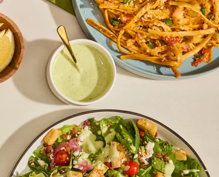 Cajun Shrimp Fettuccine noodle dish on a blue plate, next to a ramekin of green goddess dressing and the green goddess chicken cobb salad.