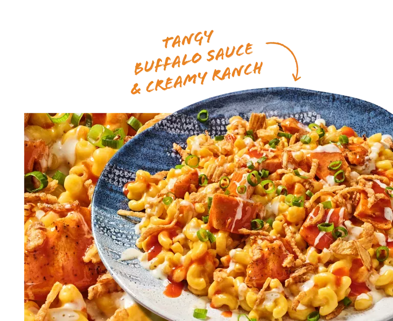 Tangy Buffalo Sauce &amp; Creamy Ranch. Noodles &amp; Company's Buffalo Chicken Ranch Mac shown on a blue plate with a close-up of cheesy noodles and chicken.