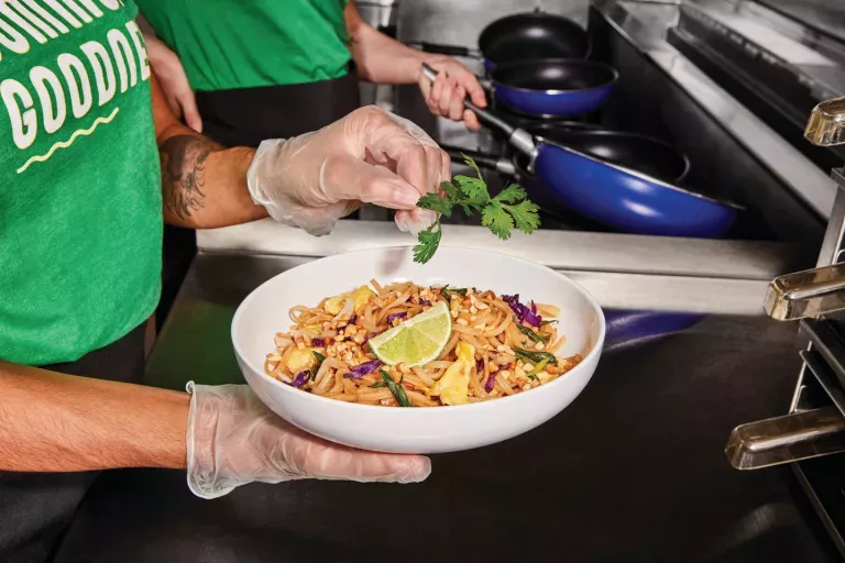Noodles &amp; Company Team Member garnishing a bowl of Pad Thai with Cilantro