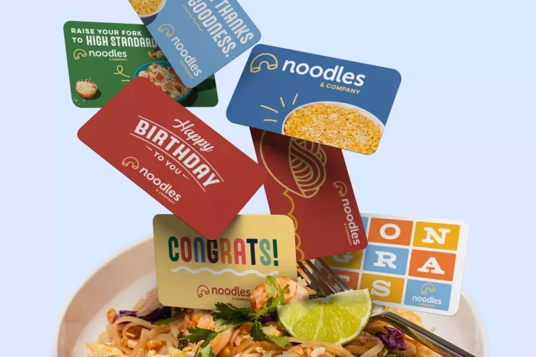Noodles &amp; Company gift cards falling into a bowl of Pad Thai.