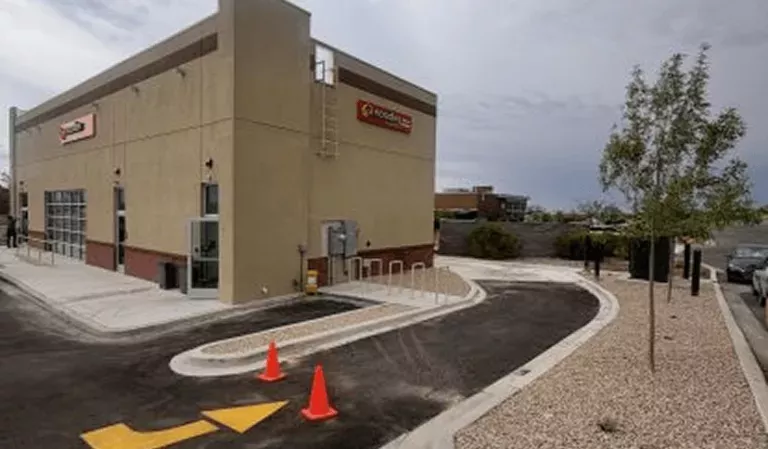 Noodles and Company building next to a tree, showing pickup window lane with a yellow arrow on the pavement and 2 traffic cones