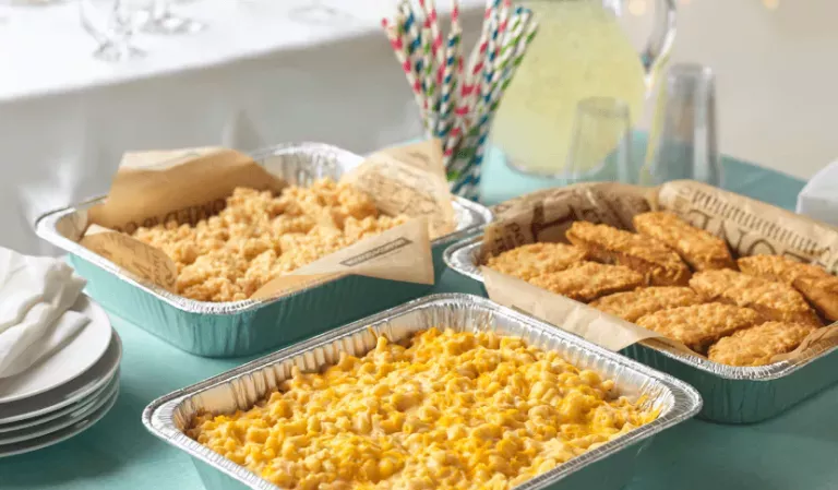 Noodles Catering Spread on a light blue tablecloth with Buttery Parmesan Noodles, Creamy Cheddar Mac &amp; Cheese, and Cheesy Garlic Bread