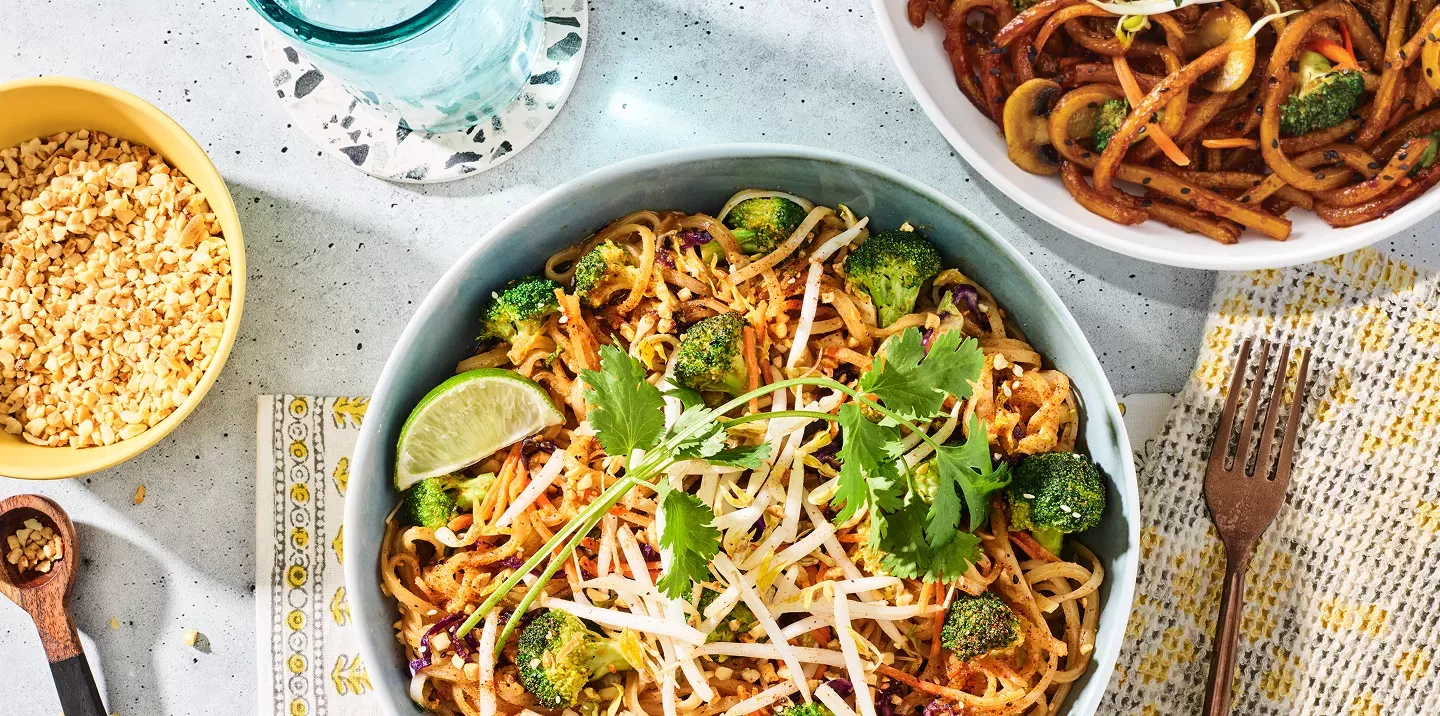 Tabletop image of Indonesian peanut chicken sauté with Japanese pan noodles and a carafe of peanuts and a fork