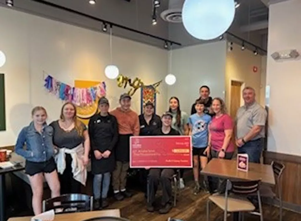 Noodles and Company 2025 Scholarship Award Winner holding a large check surrounded by friends, family and fellow employees.
