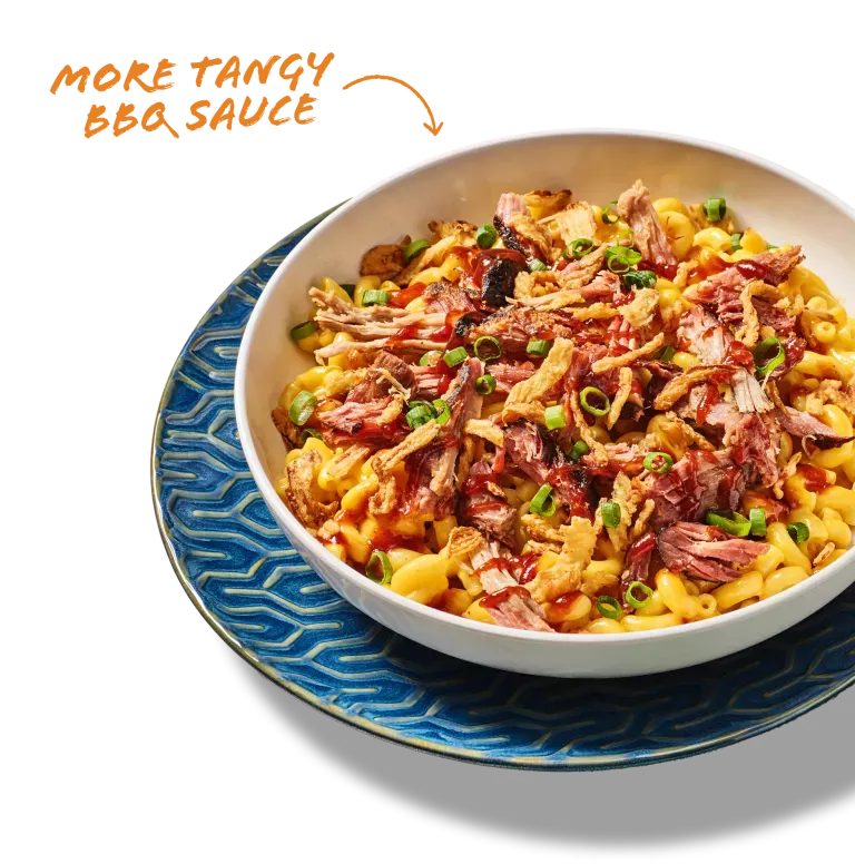 More tangy BBQ sauce. Noodles &amp; Company's Pulled Pork BBQ  Mac &amp; Cheese shown in a white bowl on a decorative blue plate.